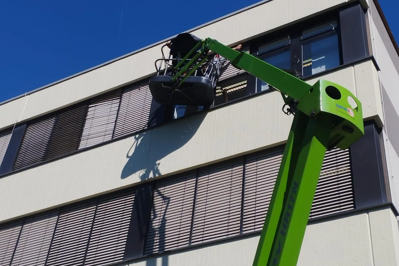 Monteur der Vatan GmbH arbeitet mit einer Hubarbeitsbühne an den Sonnenschutzelementen einer Bürofassade